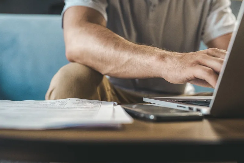 A man typing on a laptop, reviewing documents