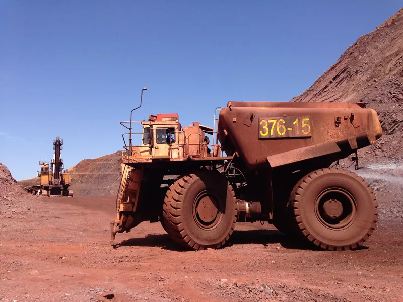 A large haul truck and an excavator work in a red-earth open-pit mine under a clear sky