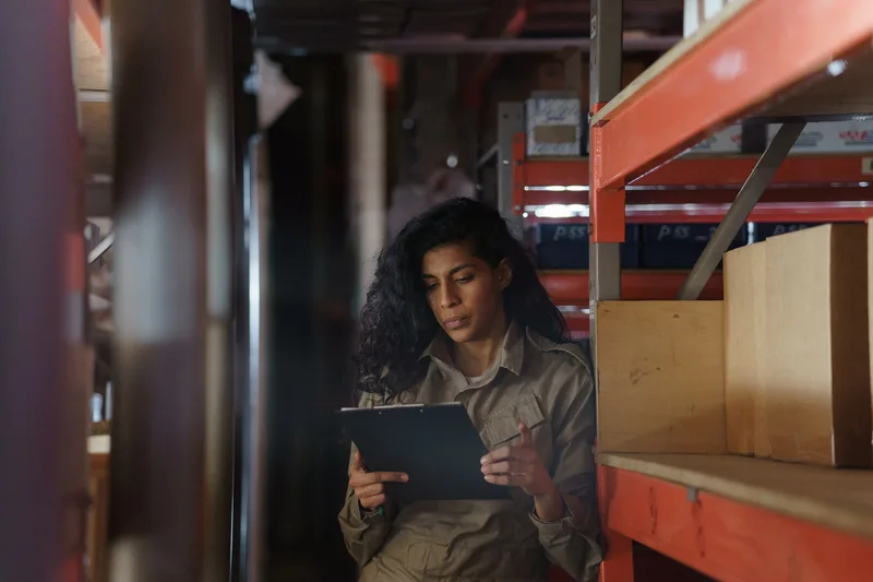 A worker takes inventory of stock in a warehouse using a clipboard