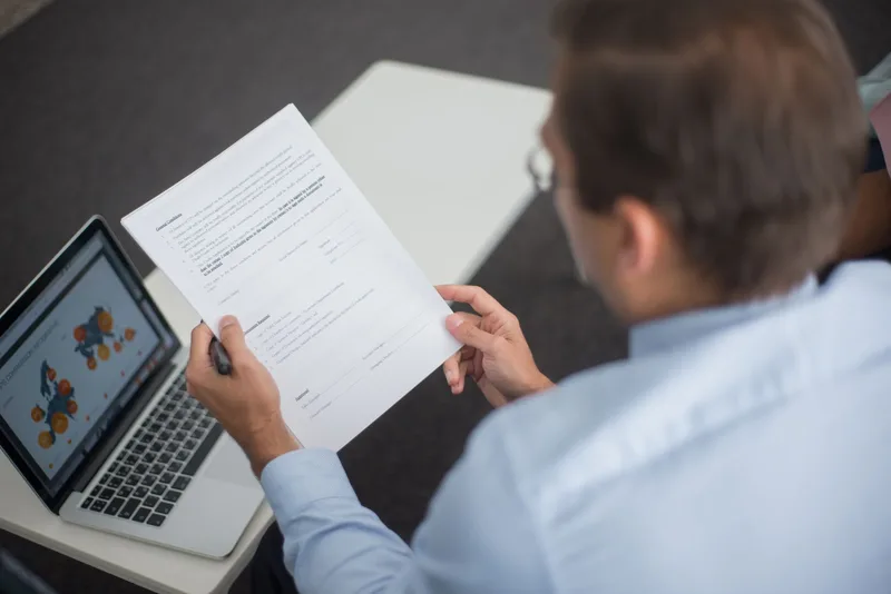 A businessperson reviewing a supplier contract document beside a laptop
