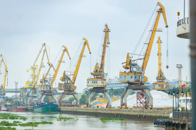 Yellow port cranes line a river waterfront beside moored cargo vessels