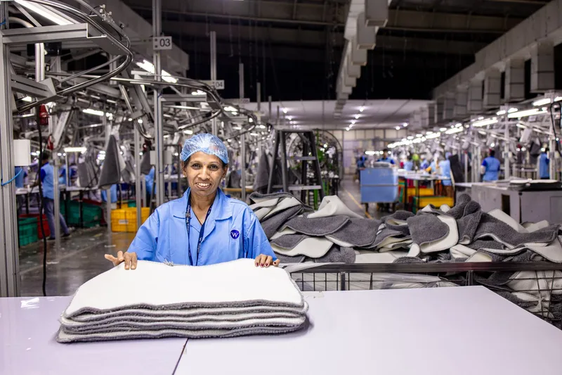 A textile worker in a factory folds products surrounded by industrial machines