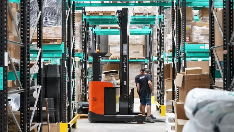 Two workers handle a package in a spacious warehouse surrounded by shelves stocked with boxes and products